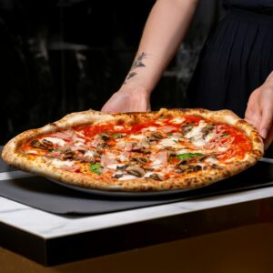 Freshly baked pizza with mushrooms and tomato sauce served on a tray by a chef.